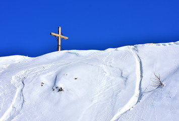 Fototapeta premium Beautiful view of the wooden cross that stands in the top of a snowy hill. With clear blue sky for the background. Vogel, Slovenia