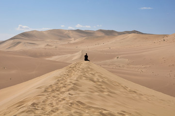 Fototapeta na wymiar Uomo seduto su una duna che osserva il deserto
