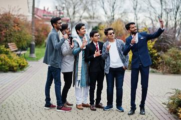 Group of six south asian indian mans in traditional, casual and business wear standing and making selfie at mobile phone together.