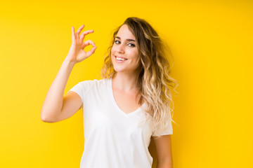 Young beautiful blonde woman over yellow background smiling positive doing ok sign with hand and fingers. Successful expression.