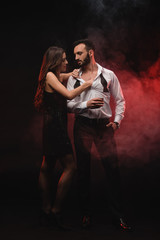 passionate woman hugging man with glass of whiskey in red smoky room