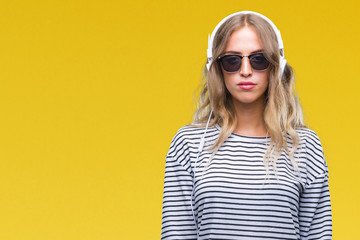 Beautiful young blonde woman wearing headphones and sunglasses over isolated background with serious expression on face. Simple and natural looking at the camera.
