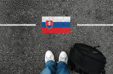 a man with a shoes and backpack is standing on asphalt next to flag of Slovakia and border