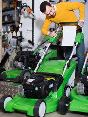 Fototapeta premium vigorous guy deciding on best lawnmower in garden equipment shop