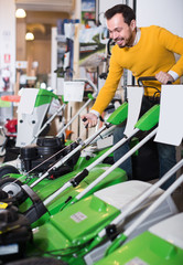Fototapeta premium attentive guy deciding on best lawnmower in garden equipment shop