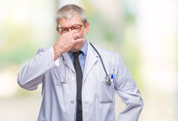 Handsome senior doctor man over isolated background smelling something stinky and disgusting, intolerable smell, holding breath with fingers on nose. Bad smells concept.