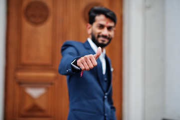 Stylish beard indian man with bindi on forehead, wear on blue suit posed outdoor against door of...