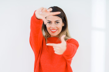 Young woman wearing casual red sweater over isolated background smiling making frame with hands and fingers with happy face. Creativity and photography concept.