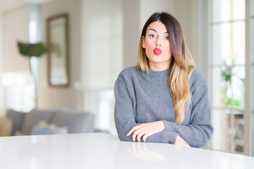 Young beautiful woman wearing winter sweater at home puffing cheeks with funny face. Mouth inflated with air, crazy expression.