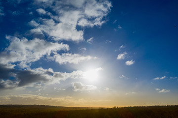 Dramatic sky with pale yeellow and brown colors under bright blue colors over a steep dark green forest.