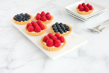 Raspberry and Blueberry Tarts on White Marble Board and Plates