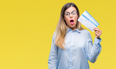 Young beautiful woman holding boarding pass over isolated background scared in shock with a...