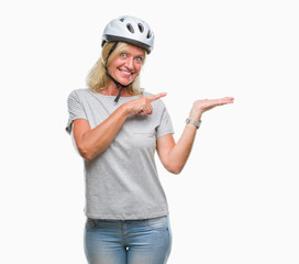 Middle age caucasian cyclist woman wearing safety helmet over isolated background amazed and smiling to the camera while presenting with hand and pointing with finger.