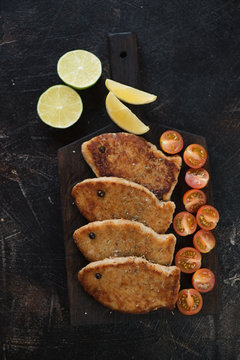 Black wooden serving board with roasted fish cutlets made of pike fillet, flatlay on a dark brown stone surface, vertical shot