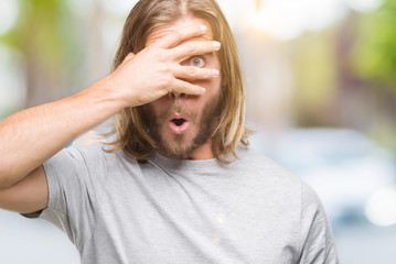Young handsome man with long hair over isolated background peeking in shock covering face and eyes with hand, looking through fingers with embarrassed expression.