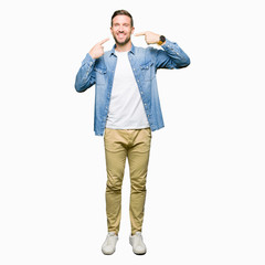 Handsome man with blue eyes and beard wearing denim jacket smiling confident showing and pointing with fingers teeth and mouth. Health concept.