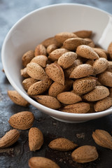 White bowl with unpeeled almonds, vertical shot, selective focus, close-up