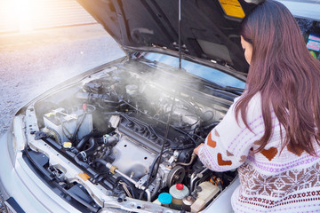 The woman stood near the car that was broken on the road while traveling in the countryside.