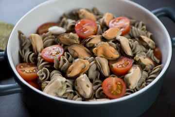 Bowl of hemp flour pasta served with mussels and cherry tomatoes, selective focus, studio shot