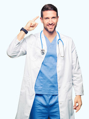 Handsome doctor man wearing medical uniform over isolated background Smiling pointing to head with one finger, great idea or thought, good memory