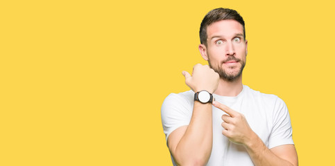 Handsome man wearing casual white t-shirt In hurry pointing to watch time, impatience, upset and...