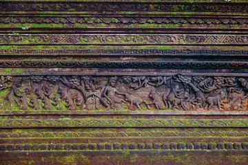 Mouldy tropical Balinese wall with traditional stone carved patterns covered with moss.