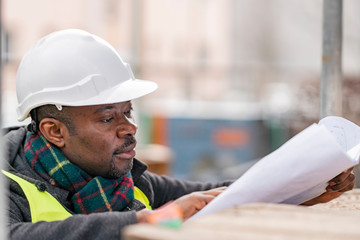 Profile portrait of an absorbed African American male engineer wearing safety jacket and helmet...