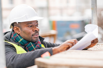 Profile portrait of an absorbed African American male engineer wearing safety jacket and helmet...