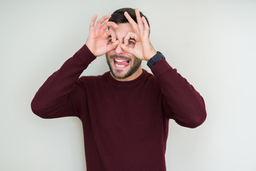 Young handsome man wearing a sweater over isolated background doing ok gesture like binoculars sticking tongue out, eyes looking through fingers. Crazy expression.