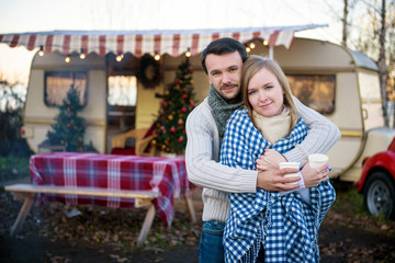 Beautiful young couple standing with hot coffee in the background of a camper van  in the autumn day.