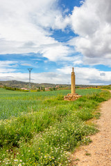 Roadside cross with scallop shells on the Way of St. James, Camino de Santiago near the village of Ventosa in La Rioja, Spain, a pilgrim in the distance