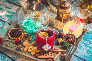 Obraz na płótnie Canvas New Year's still life with mug of tea with knitted cup cover, cookies, chocolate, dried fruit and seasonings with lights and bokeh. Photo toned and with vignette