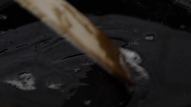 Melting lard stirred with wooden spatula in a cast iron pan. Half speed slow motion.