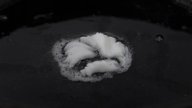 Piece of lard melting on a hot black cast iron pan. Closeup.