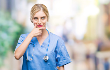 Young beautiful blonde doctor surgeon nurse woman over isolated background looking confident at the camera with smile with crossed arms and hand raised on chin. Thinking positive.