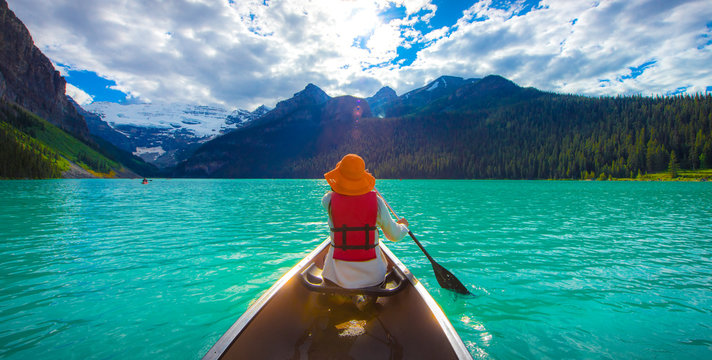 A woman in red life jacket canoeing in Lake Louise with torquoise lake and bluesky
