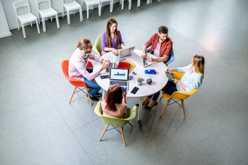 Team of a young coworkers dressed casually working together with laptops sitting at the round table...
