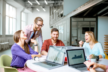 Team of a young coworkers dressed casually working together with laptops sitting at the round table in the office