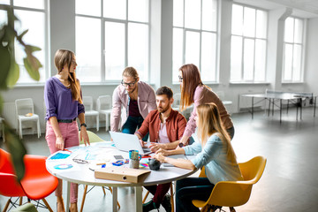 Group of a young coworkers dressed casually working together with laptops in the modern office