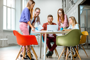 Group of a young coworkers dressed casually working together with laptops in the modern office