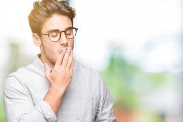 Young handsome man wearing glasses over isolated background bored yawning tired covering mouth with hand. Restless and sleepiness.