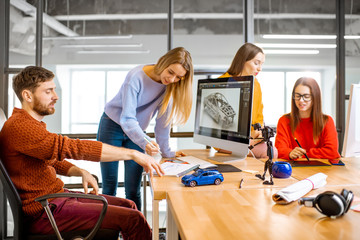 Group of young creative coworkers designing a car model at the working place with computers in the modern office interior