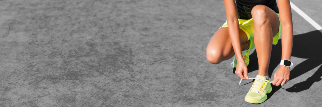 Active healthy lifestyle girl getting ready to walk on city street background grey texture. Crop of shoes and legs woman tying laces banner panorama.