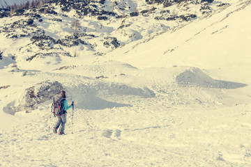 Female alpinist descending into mountain valley crossing flakes of snow.