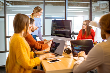 Team of a young programmers dressed casually working on computer code sitting in the modern office...