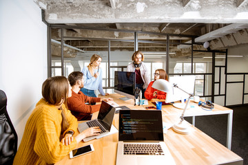 Team of a young programmers dressed casually working on computer code sitting in the modern office interior
