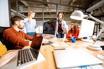 Group of young coworkers dressed casually working together on the computers in the modern office...
