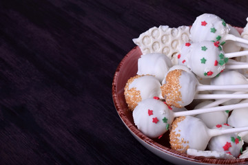 Cake pops covered in white chocolate and multicoloured sprinkles on a plate against the dark background