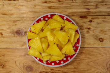 Pieces of pineapple in a plate on wooden table. Top view