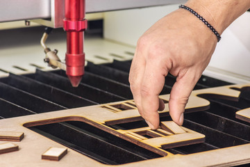 Laser engraver working and engraving wooden board with hand